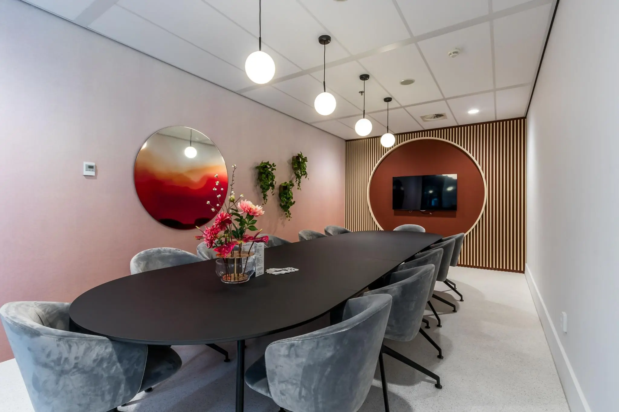 Moderne vergaderruimte aan de Vliegend Hertlaan met een lange ovale tafel, fluwelen stoelen, ronde wanddecoratie en hanglampen.